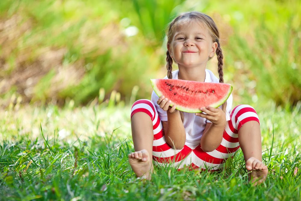 happy girl eating watermelon in grass