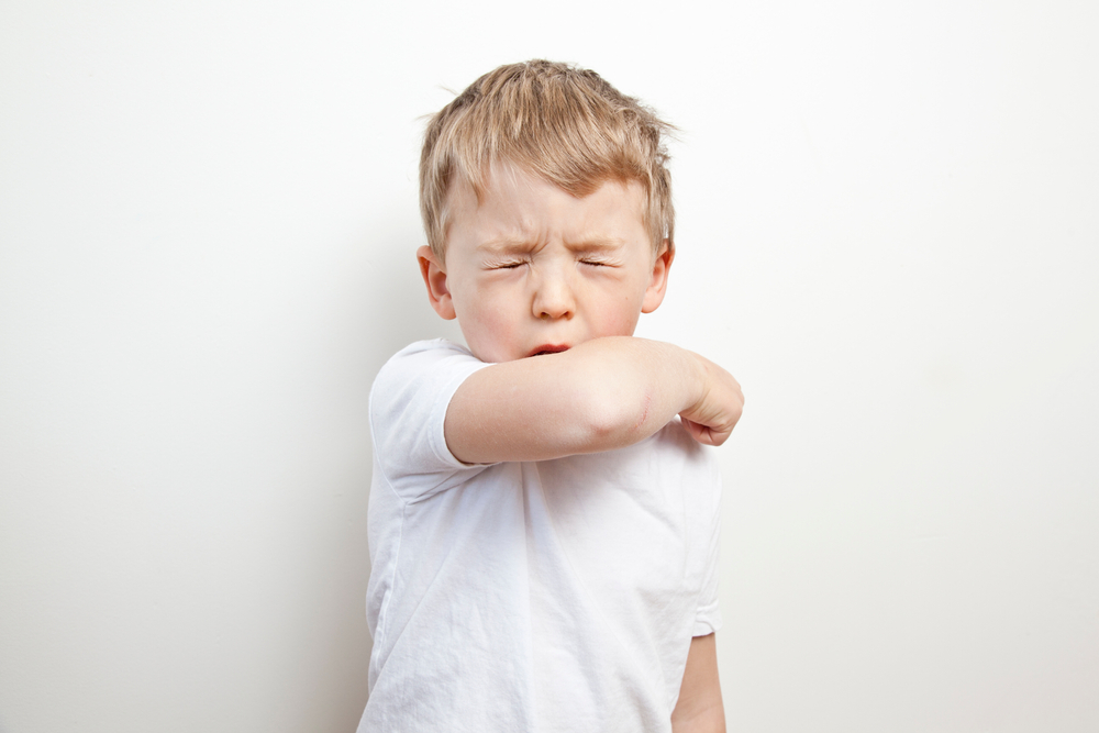 little boy coughing in his elbow