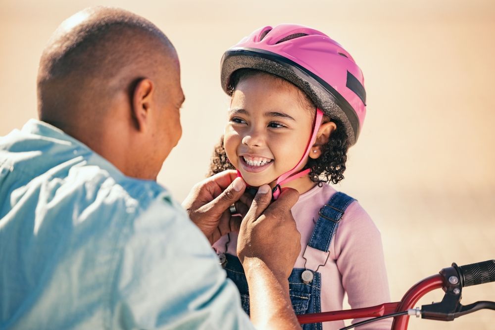 Dad helping kid put on bike helmet.